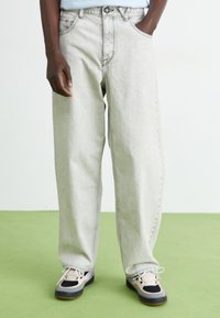 Light gray denim jeans with a relaxed fit, five-pocket design, and faded texture, paired with black and pink sneakers.