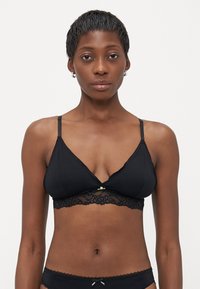 Zwarte bralette met kantafwerking, driehoekige cups, verstelbare bandjes en een decoratieve centrale accent. Glad stof met een zachte textuur.