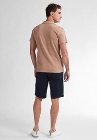 Vaalean beige pikeepaita lyhyillä hihoilla, yhdistetty tummanlaivansiniset shortsit. Valkoisissa tennareissa on beige yksityiskohta kantapäällä. Yksinkertainen, rento muotoilu.