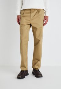 Khaki pants made of cotton blend fabric with a straight design, featuring front pleats. Paired with brown leather shoes.
