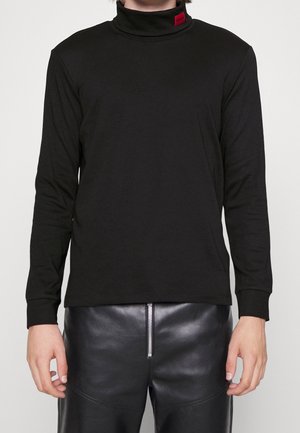 Chemise noire à manches longues avec col roulé, en tissu léger, arborant une étiquette de logo rouge sur le col et une coupe ajustée. Associée à un pantalon en cuir noir.