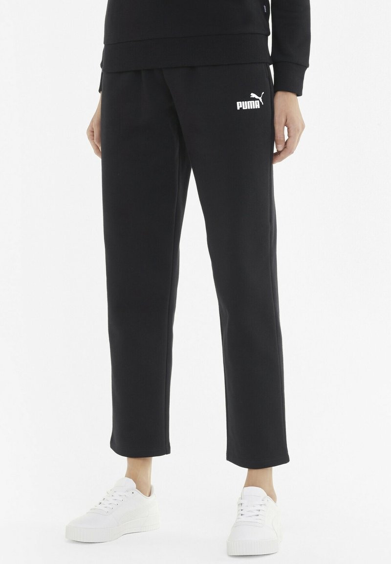 Black sweatpants with a tapered leg, made of soft fabric, featuring a white PUMA logo on the left hip and styled with white sneakers.