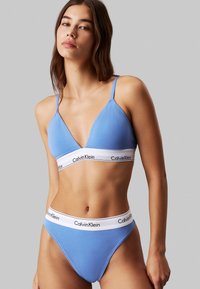 Ljusblått underklädeset med en triangulär bralette med tunna band och matchande högmidjade trosor, båda med en vit logotyp på midjebandet.