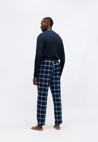 Mornarska košulja dugih rukava u kombinaciji s kariranim flanel hlačama s plavo-bijelim uzorkom. Mekani materijal, ravni kroj, elastični pojas.