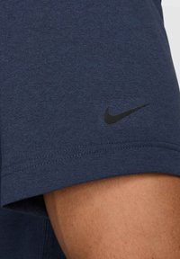 Navy blue athletic T-shirt with short sleeves, featuring a black Nike logo on the upper arm. Soft, breathable fabric with a smooth texture.