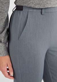 Grijze op maat gemaakte broek met een zachte textuur, voorzien van zijzakken en een elastische tailleband, gepresenteerd tegen een neutrale achtergrond.