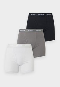 Trois boxers pour hommes en blanc, gris et noir, chacun avec une ceinture élastique de marque "Hollister".