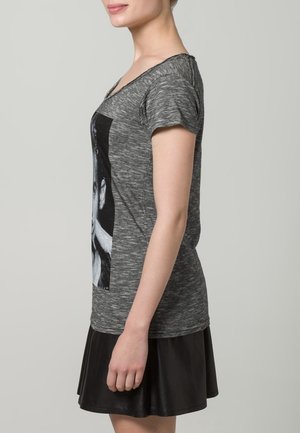 Harmaa lyhythihainen t-paita, jossa on grafiikkaprintti edessä, yhdistettynä mustaan laskostettuun hameeseen. Pehmeä kangas, rento istuvuus, casual-mallinen.