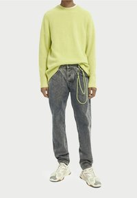 Jasnozielony sweter na drutach, luźne szare dżinsy z detalem łańcucha oraz białe trampki z szarymi akcentami. Prosty design, casualowy styl.