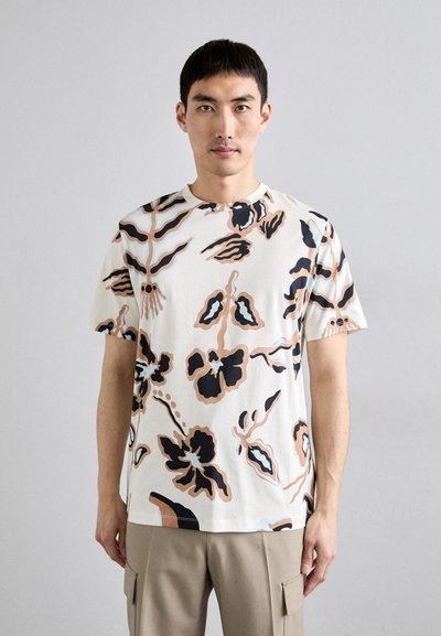 T-shirt à manches courtes crème avec des motifs floraux abstraits en noir, marron et bleu. Tissu doux, coupe décontractée, col rond.