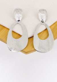 Orecchini in argento con una superficie texturizzata e ondulata. Ognuno presenta una forma ovale con un centro vuoto e un attacco superiore arrotondato.
