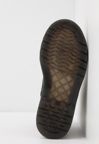 Podešev černé průhledné boty s texturovaným vzorem protiskluzu a logem se zkřížením uprostřed, na bílém pozadí.