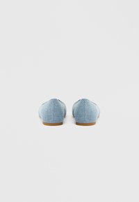 Zapatillas de tela vaquera azul claro con suela plana y textura suave, con puntera redondeada y detalles mínimos de costura.