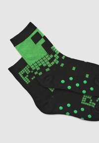 Calzini neri con un motivo pixelato verde e pois. Realizzati in materiale morbido, progettati per comfort e stile. Di lunghezza alla caviglia, accoglienti.