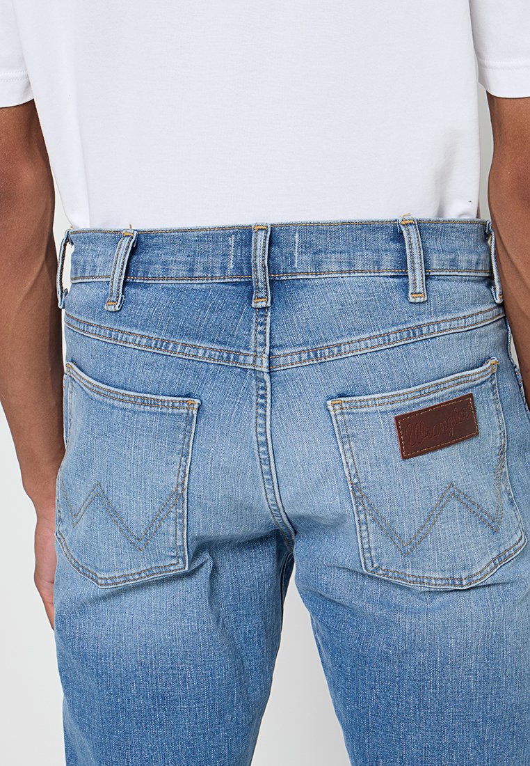 Jasnoniebieskie dżinsy o prostym kroju, z brązową skórzaną łatą i dwiema tylnymi kieszeniami z zygzakowatym przeszyciem.