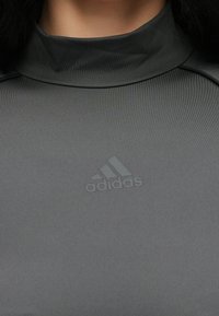 Szürke sportfelső álnyak kialakítással. Simább, nyújtható anyagból készült, mellrészen finoman dombornyomott Adidas logóval.