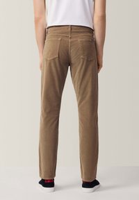 Pantaloni in corduroy marrone con design a gamba dritta, dotati di due tasche posteriori e una leggera texture. Abbinati a scarpe nere e dettagli rossi.
