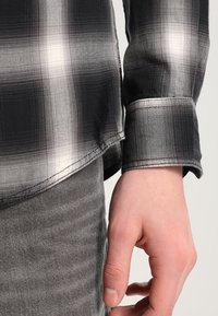 Zwarte en grijzige geruite shirt met een knoopmanschet, een gladde textuur en een afgeronde zoom, gecombineerd met grijze denim jeans.