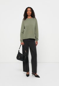 Olijfgroene sweatshirt met ronde hals en lange mouwen, gecombineerd met hoogwaardig zwarte wijde jeans met hoge taille en een zwarte handtas met gouden accenten.