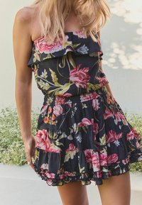 Květinový dvoudílný outfit s černým pozadím, volánkovým topem bez ramínek a vrstvenou sukní se zvonovým střihem, zdobenou živými růžovými a zelenými vzory.