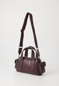 Borsa a mano in pelle color bordeaux con doppio manico superiore e una tracolla removibile, dotata di chiusura con zip e tasca laterale.
