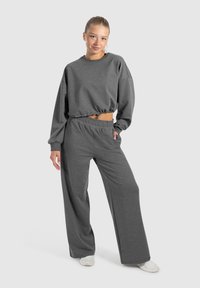 Grå cropped sweatshirt med elastisk kant og lange ærmer, parret med matchende løstsiddende sweatpants med elastisk talje.
