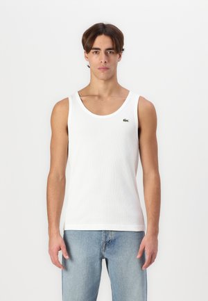 Top in cotone bianco senza maniche con una texture a coste e scollo rotondo, caratterizzato da un piccolo logo verde Lacoste sul lato sinistro del petto.