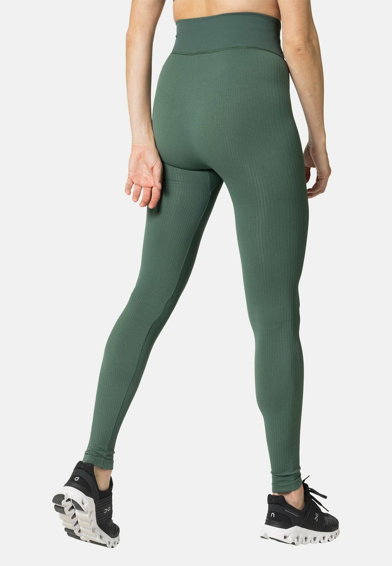 Grüne gerippte Leggings mit hohem Bund, taillierter Passform und nahtloser Textur. Kombiniert mit schwarzen Sportschuhen mit auffälligen Sohlen.