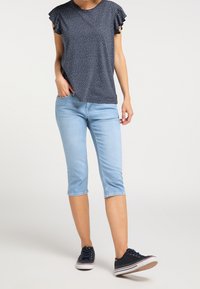 Marinblus med prickar och korta volangärmar, tillsammans med ljusblå cropped jeans och marinblå sneakers med vita sulor.