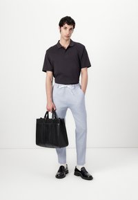 Svart polo skjorte, lyseblå bukser og svart lær tote-bag. Svart loafers med lav hæl. Bakgrunnen er helt hvit.