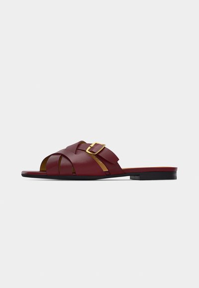 Sandale plate en cuir bordeaux avec des brides croisées et une boucle dorée sur le côté, ainsi qu'une semelle basse noire.