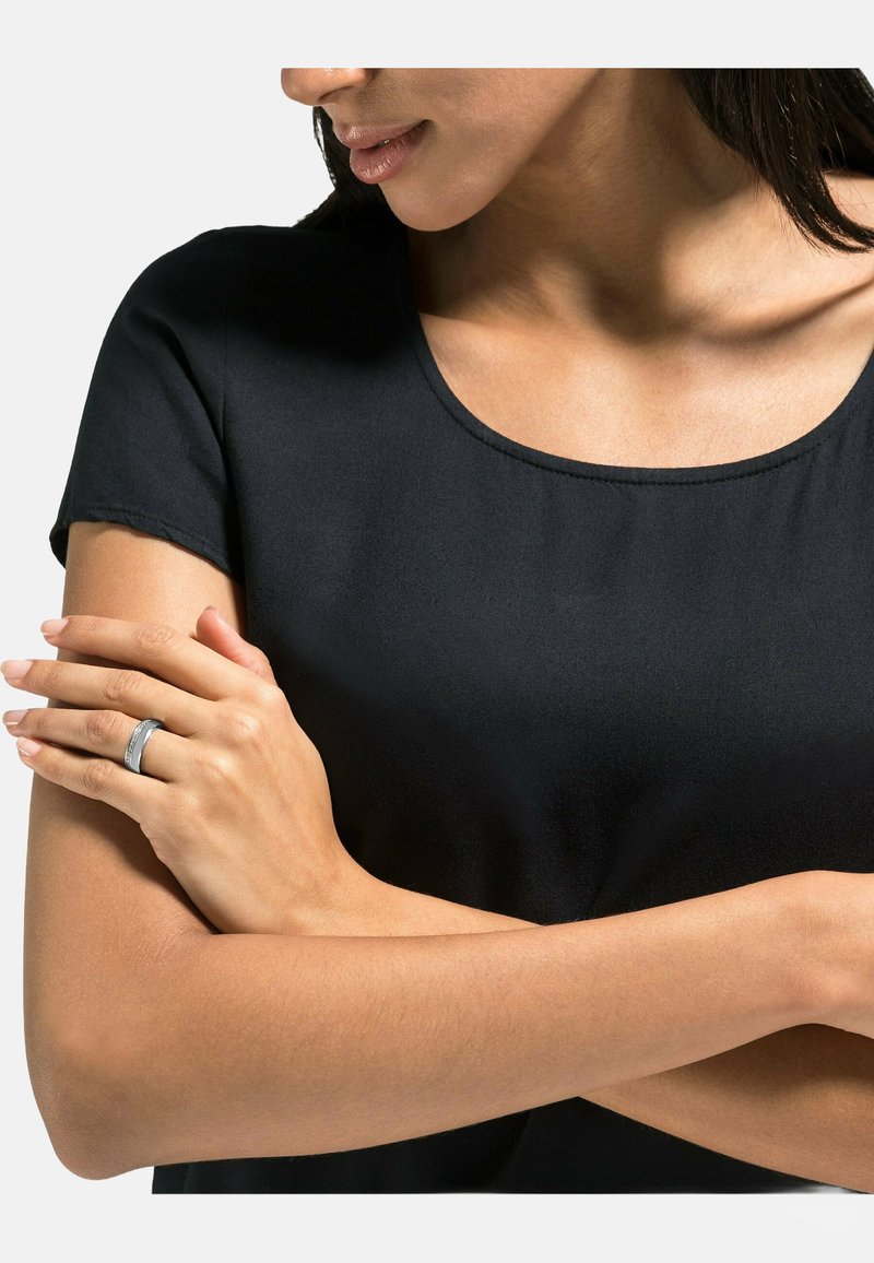 Top nero a maniche corte con scollatura a girocollo, tessuto morbido e vestibilità aderente. Un anello argento sulla mano aggiunge un dettaglio metallico a contrasto.
