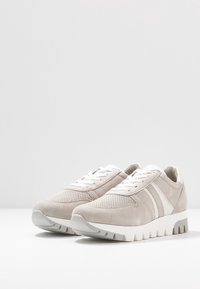 Pari harmaat mokkasneakerit valkoisilla nauhoilla, raidallisilla sivuaksenteilla, rei'itetyllä varpaalla ja paksuilla valkoisilla urilla valkoisella pinnalla.