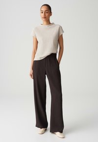 Cream textured short-sleeve top, high neckline, paired with loose-fitting black pleated trousers and light-colored slip-on shoes.