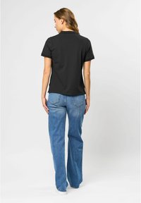 Zwarte polo met korte mouwen en rechte snit, gecombineerd met losse blauwe denim jeans. Zichtbare achterste stiknaden en details van de tailleband.