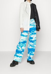 Valkoinen ja musta kaksivärinen nappipaita yhdistettynä sinisiin pilvimallisiin ylisuuriin housuihin. Mustat platform-kengät ja pieni olkalaukku.