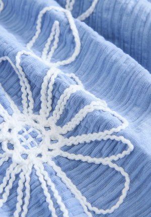 Ljusblått tyg med vit broderad blommönster med tjocka konturer, texturerade ribbor och ett vävt center.
