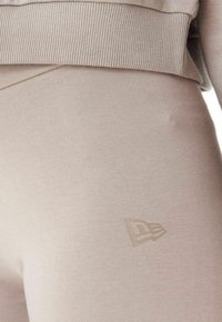 Leggings de sport beiges avec une taille côtelée, fabriqués à partir d'un tissu lisse. Présente un logo subtil de la même couleur sur la cuisse.