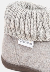 Pantofole grigie in feltro con un top a collare a maglia color crema. Include un'etichetta in tessuto con il logo "Gottstein". Texture liscia, forma rotonda.