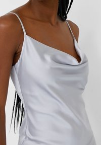 Camisole en satin gris clair avec un décolleté drapé et de fines bretelles spaghetti, mettant en valeur une texture lisse et un éclat subtil.