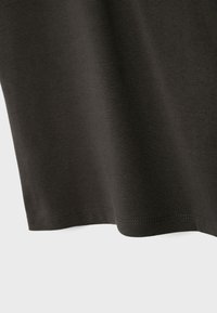 Mørkebrun stof med synlig tekstur og jævne syninger langs den nederste kant, hængende mod en ensartet lys baggrund.