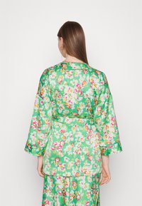 Kwiatowa zielona szata z długimi rękawami, związywana w pasie, ozdobiona żywymi różowymi, żółtymi i białymi kwiatami, z gładkiego materiału i lekko usztywnionym fasonem.