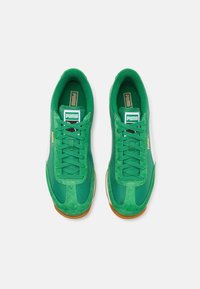 Zielone sneakersy z zamszową i materiałową cholewką, z czarnymi sznurowadłami, białym paskiem po boku oraz gumową podeszwą. Ozdobione logo Puma.