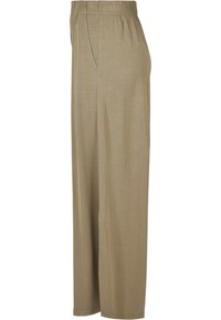 Pantalon beige coupe ample avec une taille élastique et des poches latérales, montré de profil sur fond blanc.