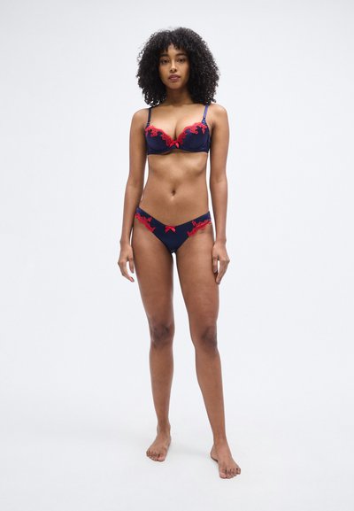 Σετ μπικίνι σε σκούρο μπλε με δαντέλα, που περιλαμβάνει στηθόδεσμο με επένδυση και κόκκινες λεπτομέρειες, καθώς και εσώρουχα με χαμηλή μέση, με περίτεχνα λουλουδένια σχέδια.