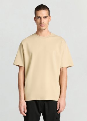 T-shirt beige a maniche corte realizzata in tessuto liscio con scollo rotondo e vestibilità rilassata, abbinata a pantaloni neri.