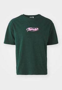 Mørkegrønn bomull T-skjorte med rund hals og korte ermer, som har et rosa grafisk logo på brystet. Glatt tekstur.