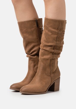 Bottes en daim marron hauteur genou avec un design flou, dotées de coutures décoratives, d'une fermeture éclair sur le côté et d'un talon carré.
