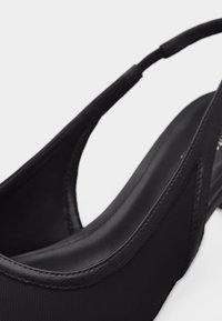 Chaussure à bride arrière pour femme noire avec bout pointu et talon bas, combinant des matériaux lisses et texturés.