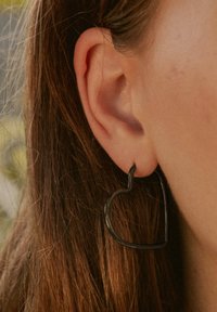 Schwarze Herz-hoop-Ohrringe aus Metall, mit strukturiertem Design, hängen vom Ohrläppchen, mittlere Dicke und glänzende Oberfläche.
